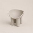 A minimalist, modern low PE stool with a rounded, bowl-like seat and four cylindrical legs, finished in a matte light gray color, set against a solid light beige background.