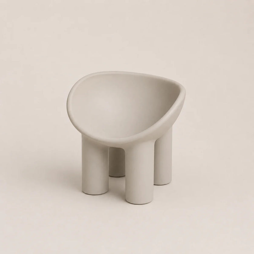 A minimalist, modern low PE stool with a rounded, bowl-like seat and four cylindrical legs, finished in a matte light gray color, set against a solid light beige background.