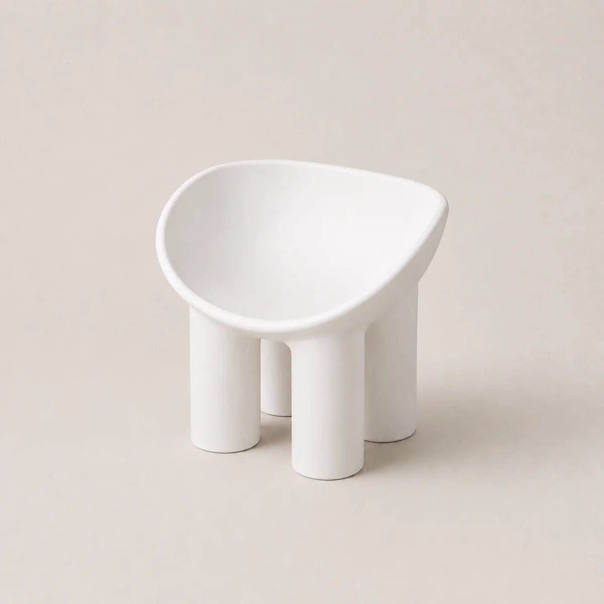 A minimalist white PE molded stool with four cylindrical legs and a rounded, asymmetrical seat, shown on a warm beige background.