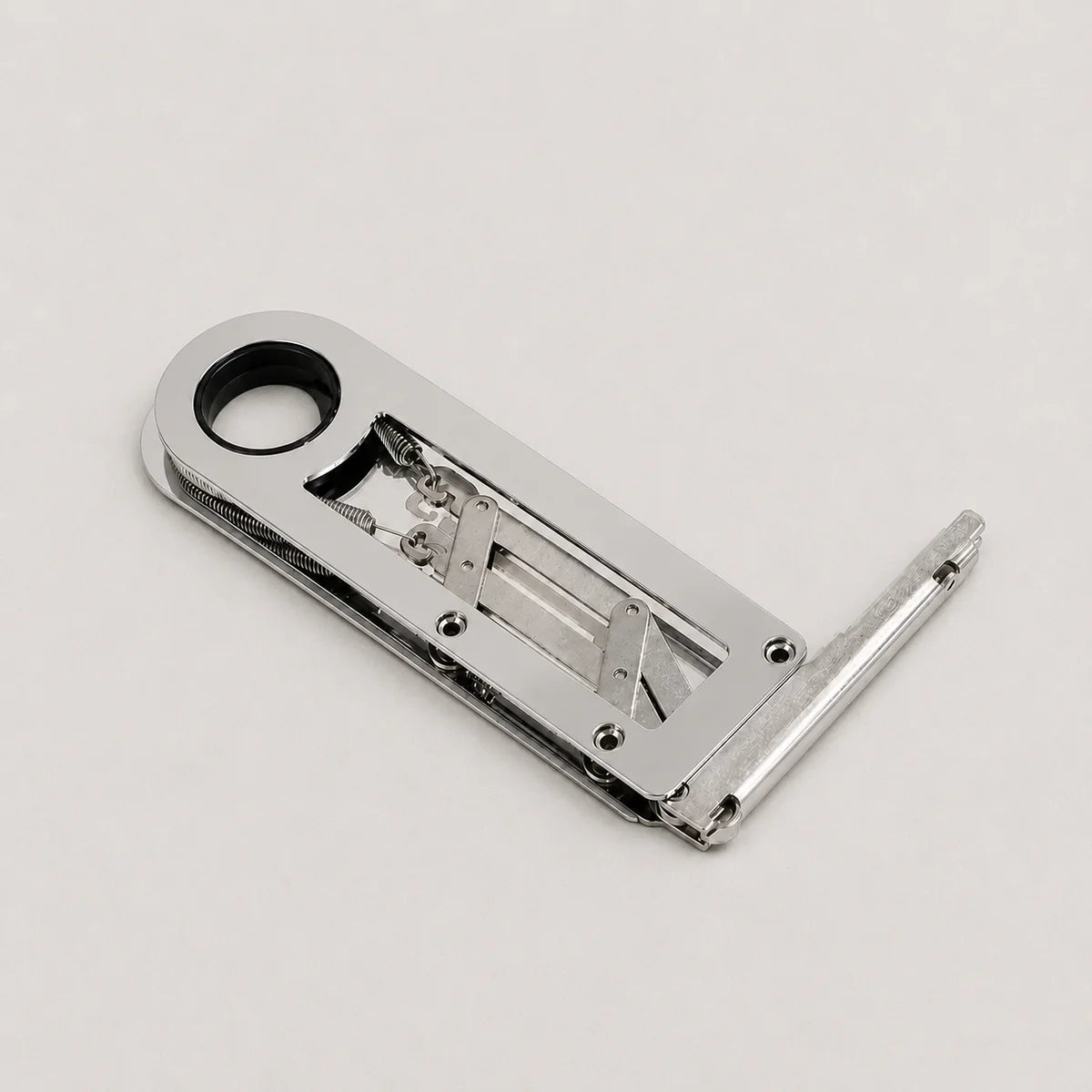 A polished silver metal latch or lock mechanism with a circular hole in the top-left and a bent extension on the right, photographed on a clean light gray background.