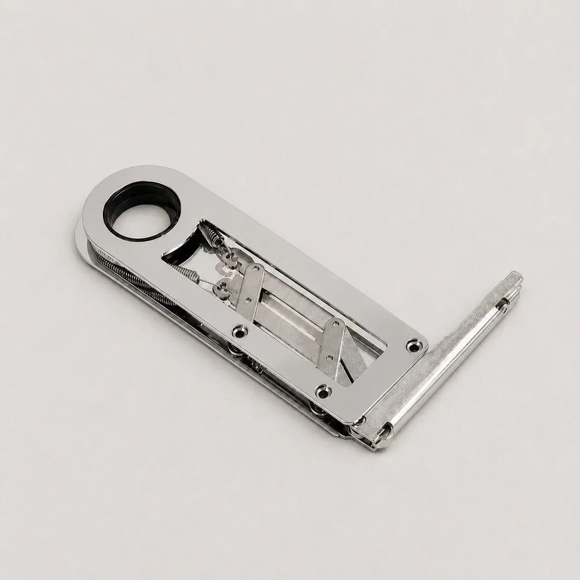 A polished silver metal latch or lock mechanism with a circular hole in the top-left and a bent extension on the right, photographed on a clean light gray background.