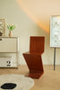 Wooden chair in a room with a light-colored wall, a small table with a vase of flowers, and a lamp.