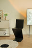 Modern black wooden chair in a minimalistic room with a light-colored wall and wooden floor.