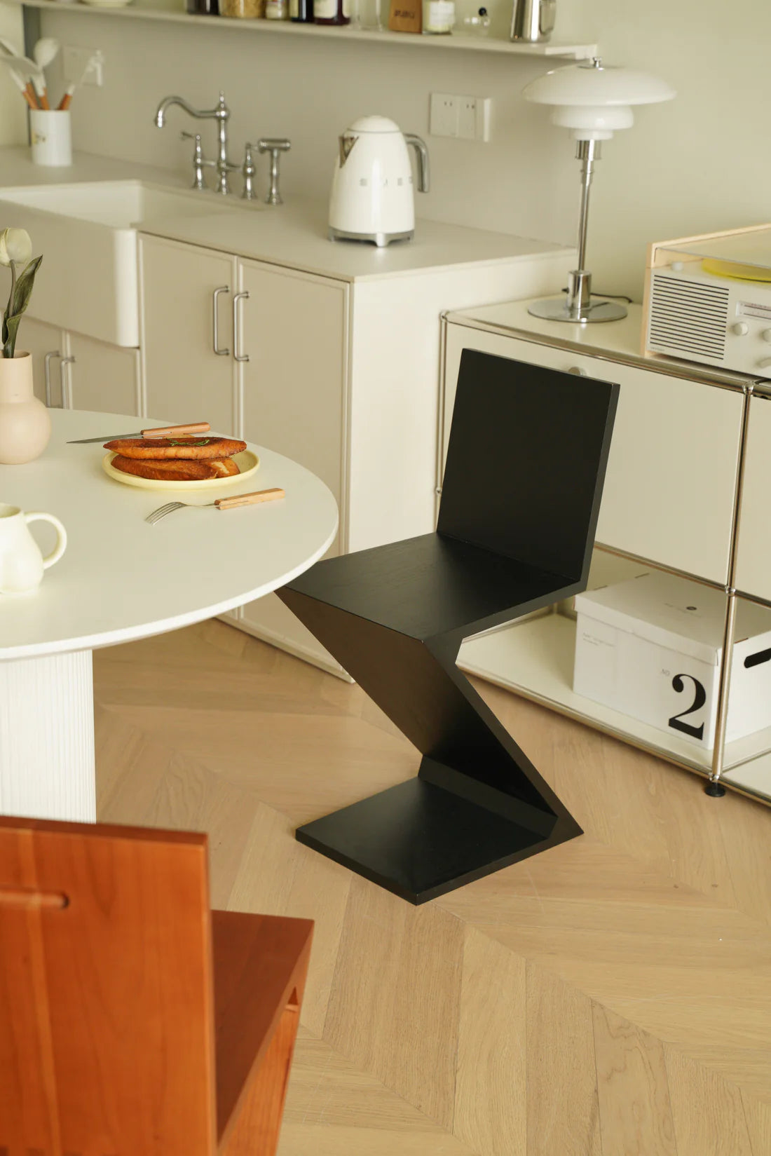 Modern kitchen with a black zigzag wooden chair, white countertop, and wooden floor.