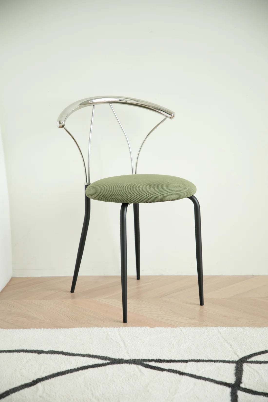 Metal dining room chair with green cushion on a wooden floor and light-colored wall background