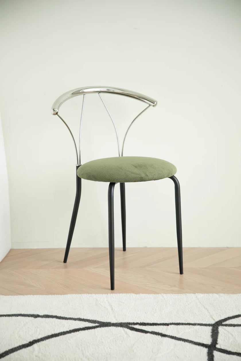 Metal dining room chair with green cushion on a wooden floor and light-colored wall background