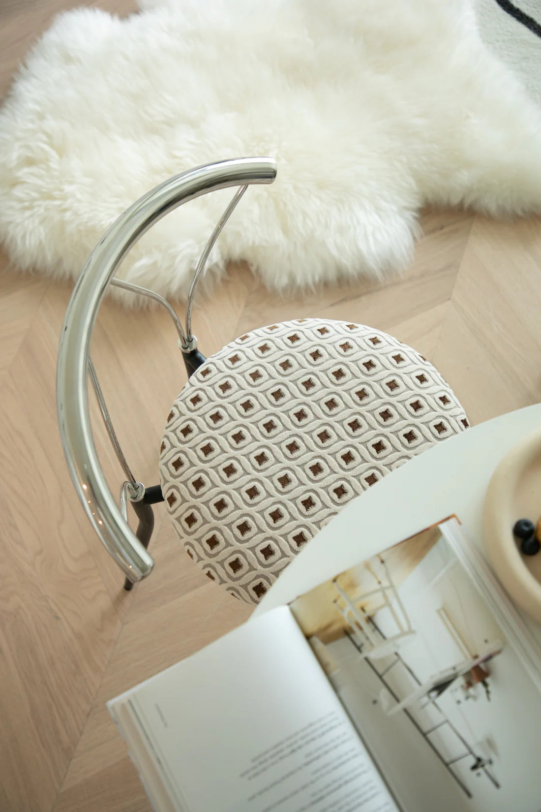 Close-up of a metal chair with a patterned backrest and armrest, next to an open book on a wooden floor.