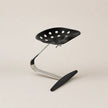 Black stool with perforated seat and curved metal frame on a beige background
