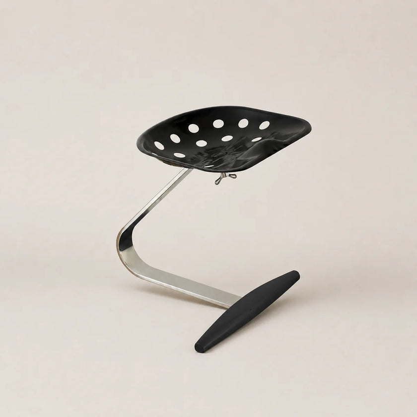 Black stool with perforated seat and curved metal frame on a beige background