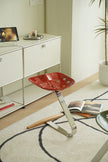 Red metal stool with a unique design in a room with a shelf and books.