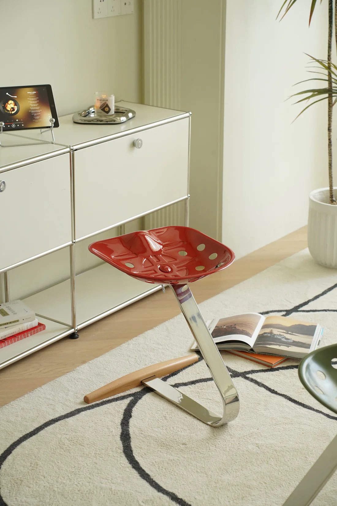 Red metal stool with a unique design in a room with a shelf and books.