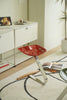 Red metal stool with a unique design in a room with a shelf and books.