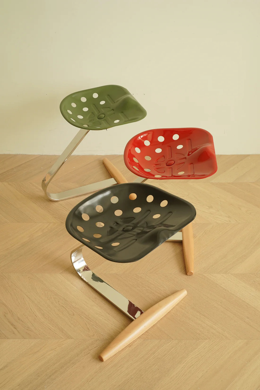 Set of three perforated stools in green, red, and black on a wooden floor.