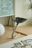 Modern black stool with metal legs on a wooden floor, next to a white spherical object and a plant.