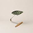 Green leaf-shaped stool with a wooden footrest on a beige background