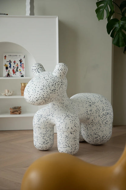 Speckled white and gray decorative animal figure kids stool on a wooden floor with a shelf in the background.