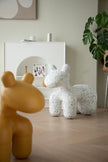 Two plastic kids chair sculptures, one yellow and one white with black speckles, on a wooden floor.
