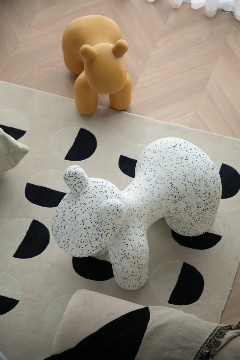 White speckled animal-shaped kids chair on a patterned rug with a yellow kids toy in the background.