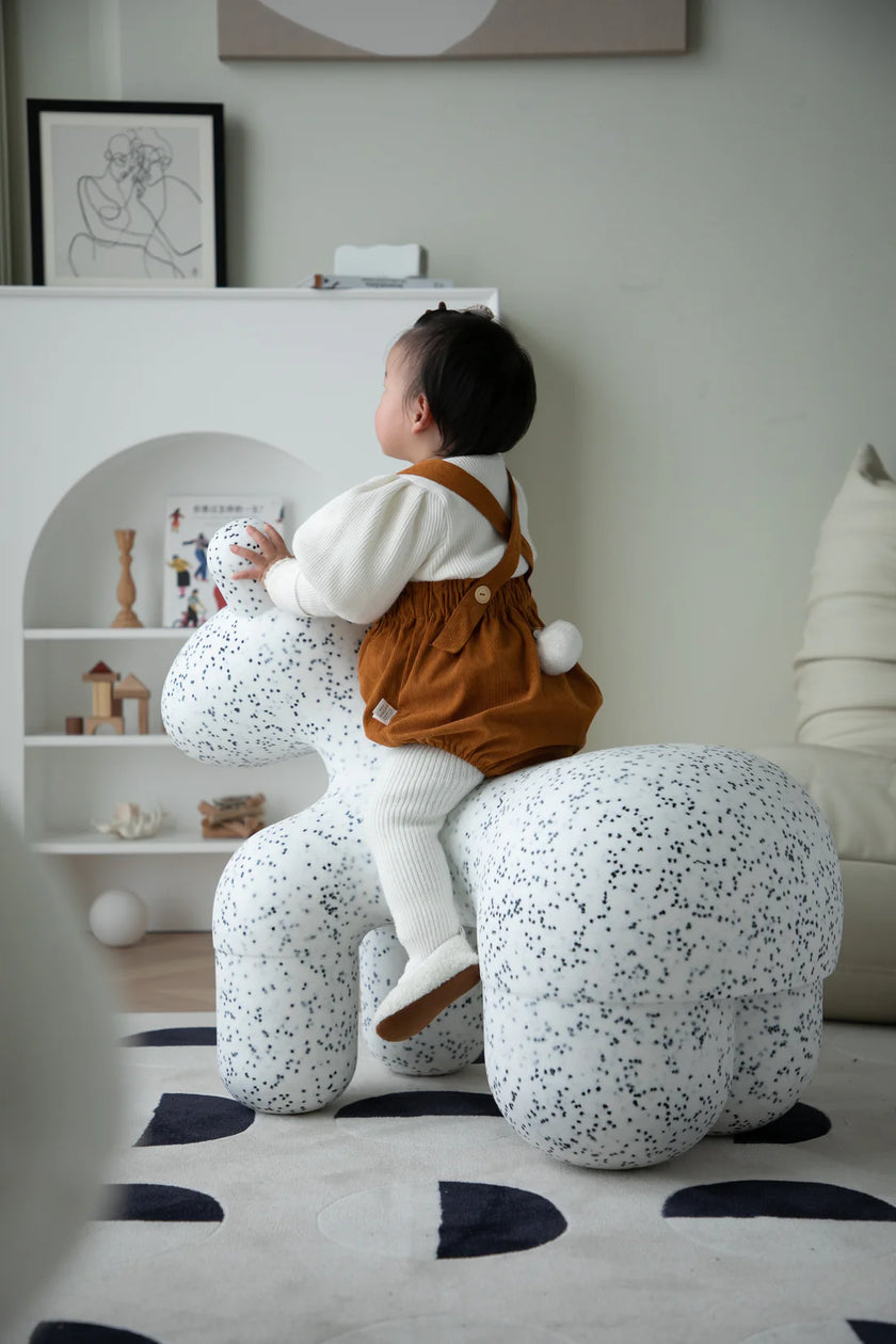 Child sitting on a speckled plastic chair in a room with shelves and decor.