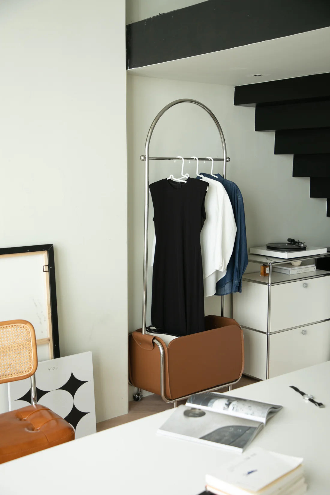 Modern interior with a clothing coat hanger dresses, a chair, and a desk with books and a pen.