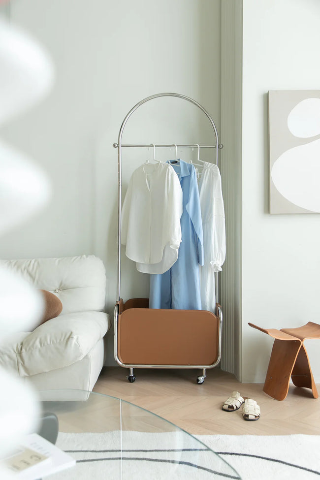 Clothing modern coat rack with clothes in a room with a white sofa and abstract art on the wall.