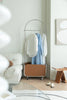 Clothing modern coat rack with clothes in a room with a white sofa and abstract art on the wall.