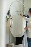 Lady hanging a white shirt on a modern metal clothing rack in a room.