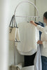 Lady hanging a white shirt on a modern metal clothing rack in a room.