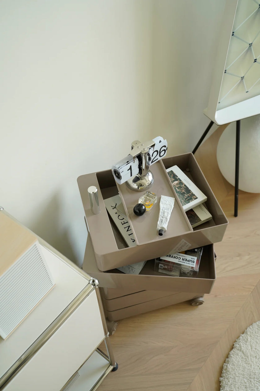 Small rolling cart with drawers with various items on a light wood floor.