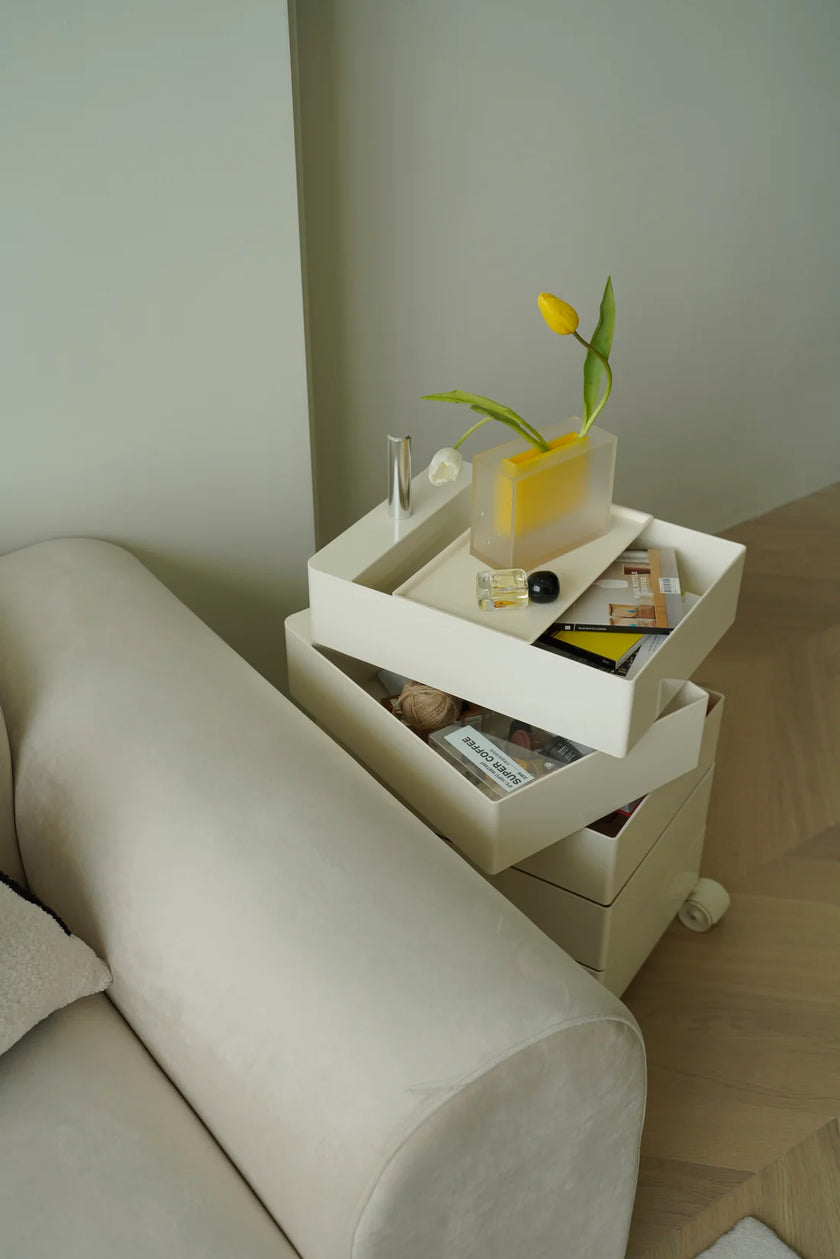 White storage containers 10 drawer rolling side table with decorative items next to a beige sofa.