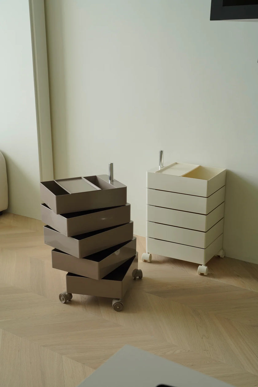 Stack of boxes on a storage wheeled cart next to a white storage unit in a room with light-colored flooring.