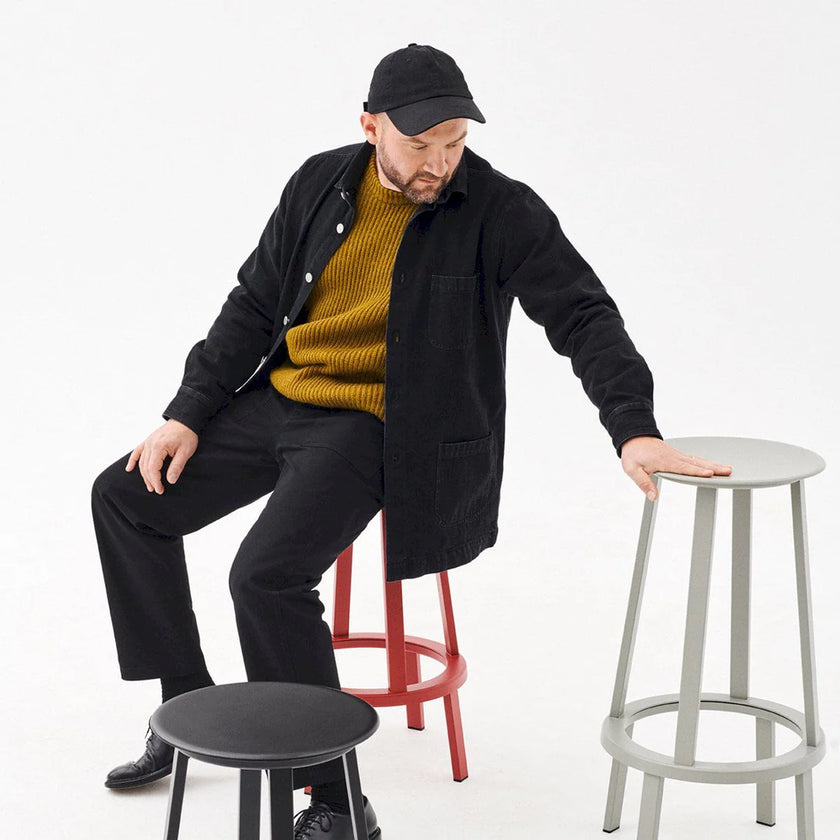 Man sitting on a black stool with three other stools in different colors on a white background