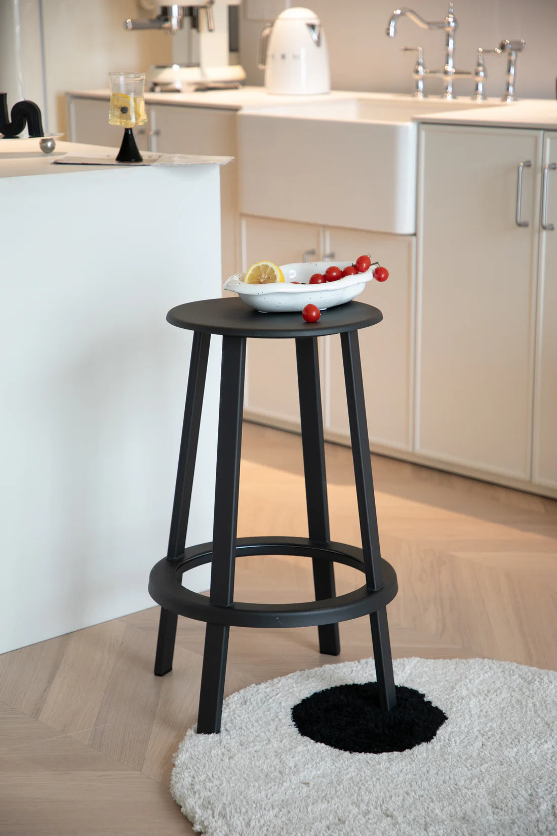 Black bar stool in a kitchen setting with a bowl of fruit on a white countertop.