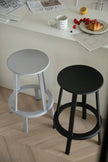 Two bar stools, one gray and one black, on a wooden floor with a table and food items in the background.