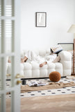 Lady lying on a white reclining sofa in a modern living room with a lamp and decor items.