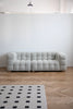 Gray love seat sofa in a room with a white wall and wooden floor.