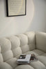 Beige reclining sofa with a magazine on it, framed text on the wall.