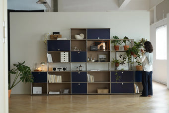 Lady interacting with a large inspired recreation USM modular metal bookshelf in a living  room.