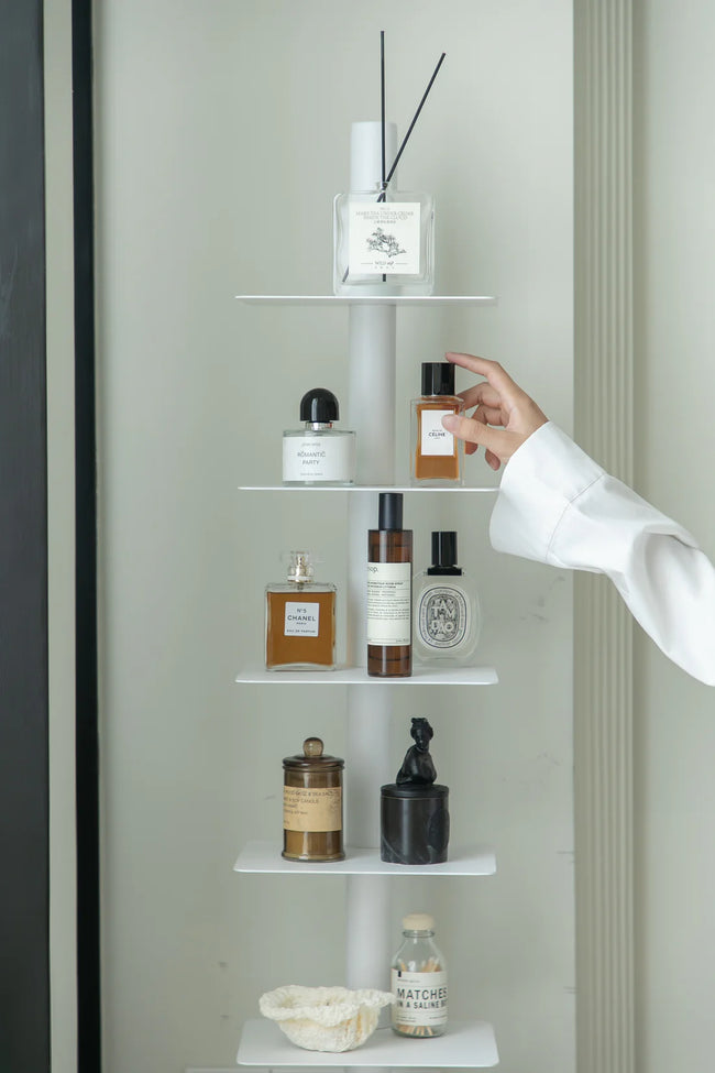 Hand reaching for a bottle on a white metal corner trinket shelf with various items