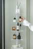 Hand reaching for a bottle on a white metal corner trinket shelf with various items