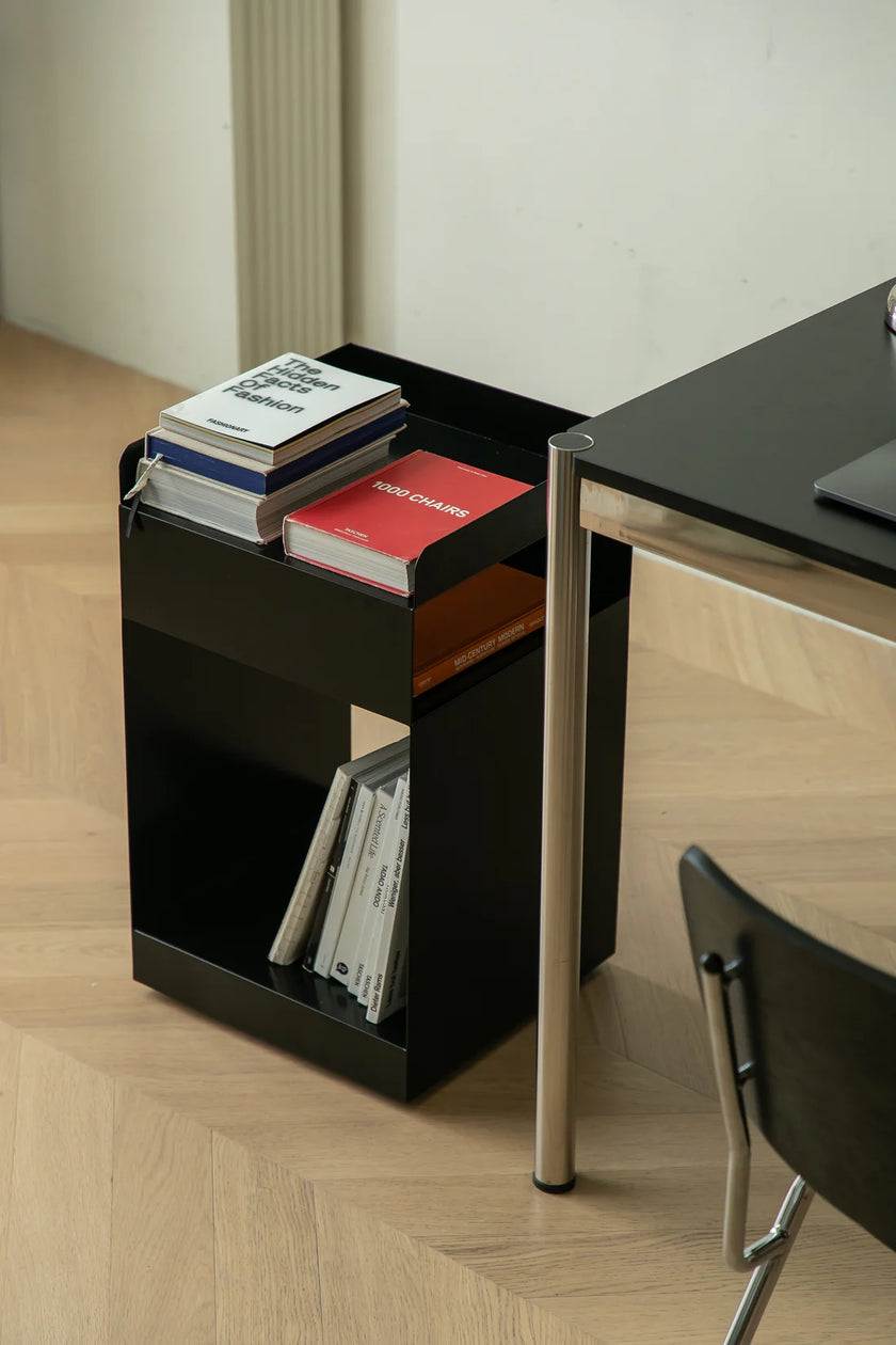 Black side table with books next to a desk in a room.