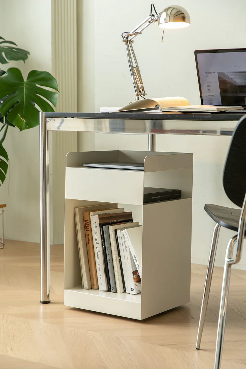 Modern white side table with books, a laptop, and a lamp in a bright room.
