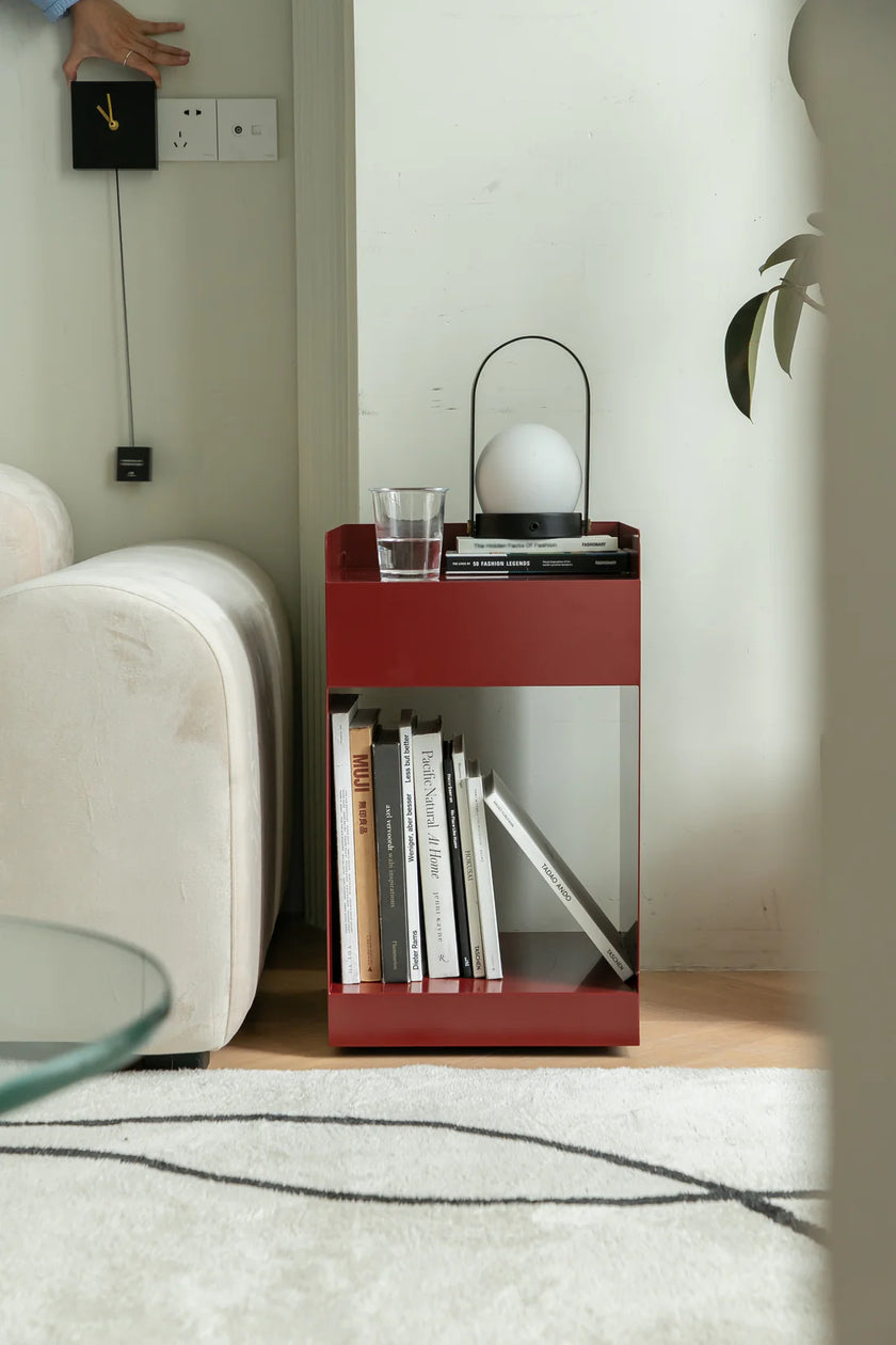 Red sofa side table with books and a glass next to a white sofa in a room.