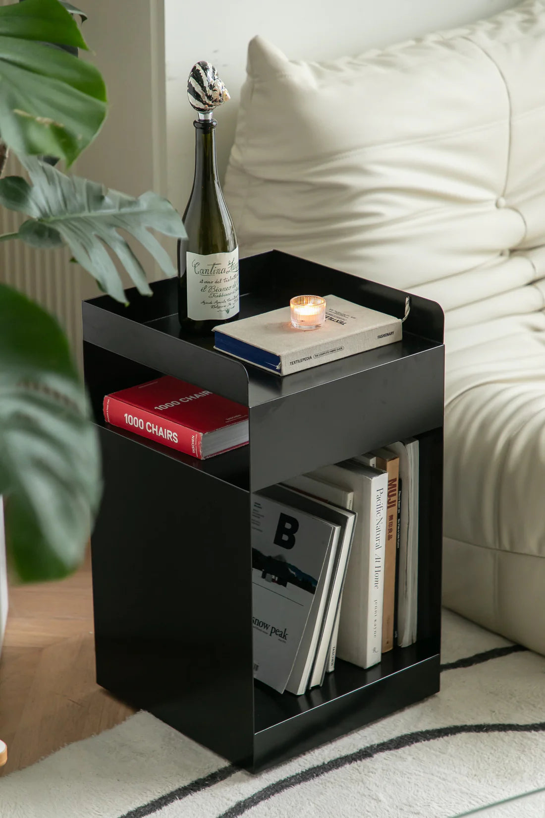 Black side table with books and a bottle in a living room setting.