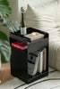 Black side table with books and a bottle in a living room setting.