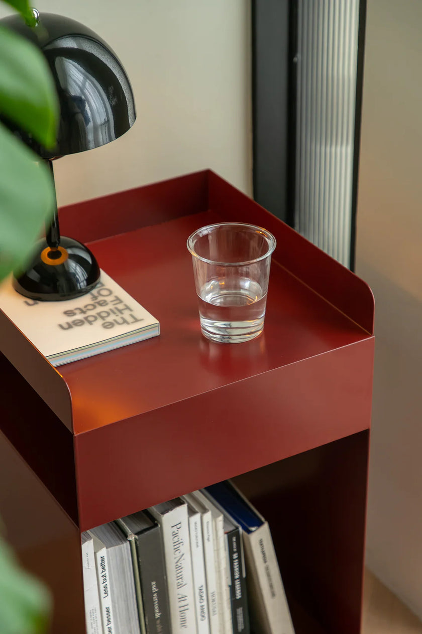 Red bed side table with a glass of water and books on a neutral background