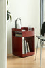 Red small side table with books, a glass, and a white object in a room with a plant and chair.