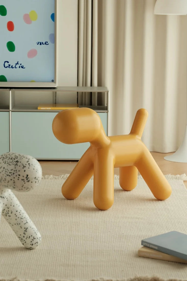 A mustard yellow, dog-shaped side table or stool made of smooth matte material, styled in a modern, warm-toned room on a textured cream rug.
