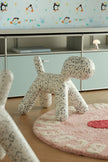 A dog-shaped white chair with black speckles, styled in a children's room with a pink rug, light wood floor, and pale blue cabinets in the background.