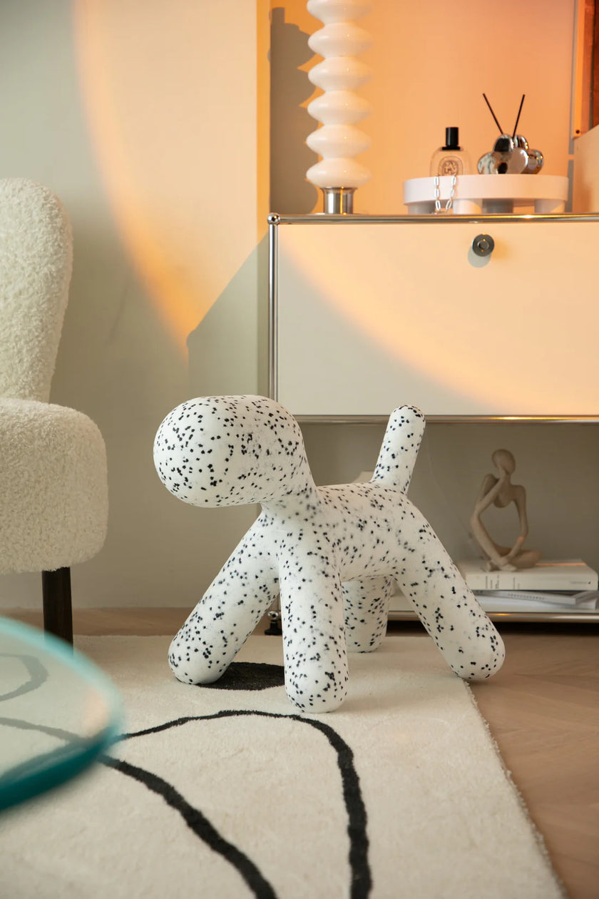 White dog-shaped cushion with black spots plastic kids chair on a rug in a room setting.
